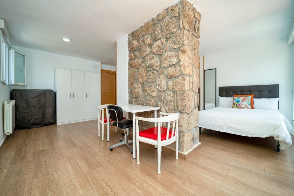 Spacious bedroom showcasing a stone wall divider, contemporary furniture, and wooden flooring with ample natural light.